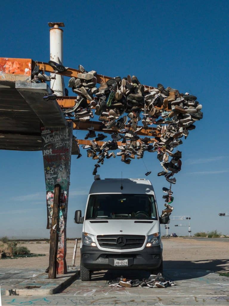 The white Sprinter van parks under an awning covered with undreds and hundreds of shoes.