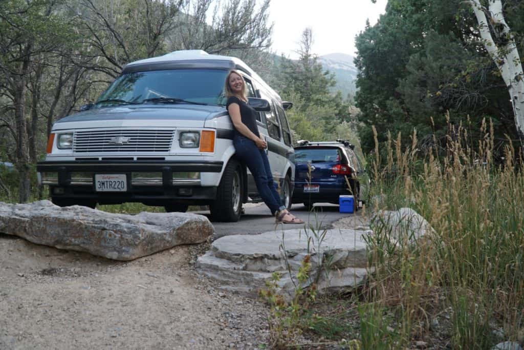 Girl casually leans against her van in the woods.