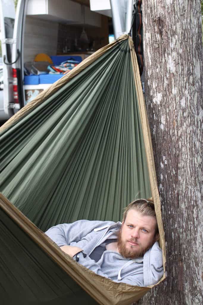 Guy chills in a hammock. The van sits in the background.