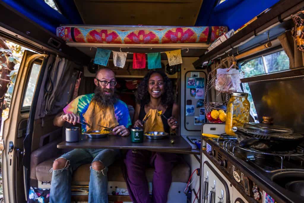 man and woman eat at fold out table inside vw campervan