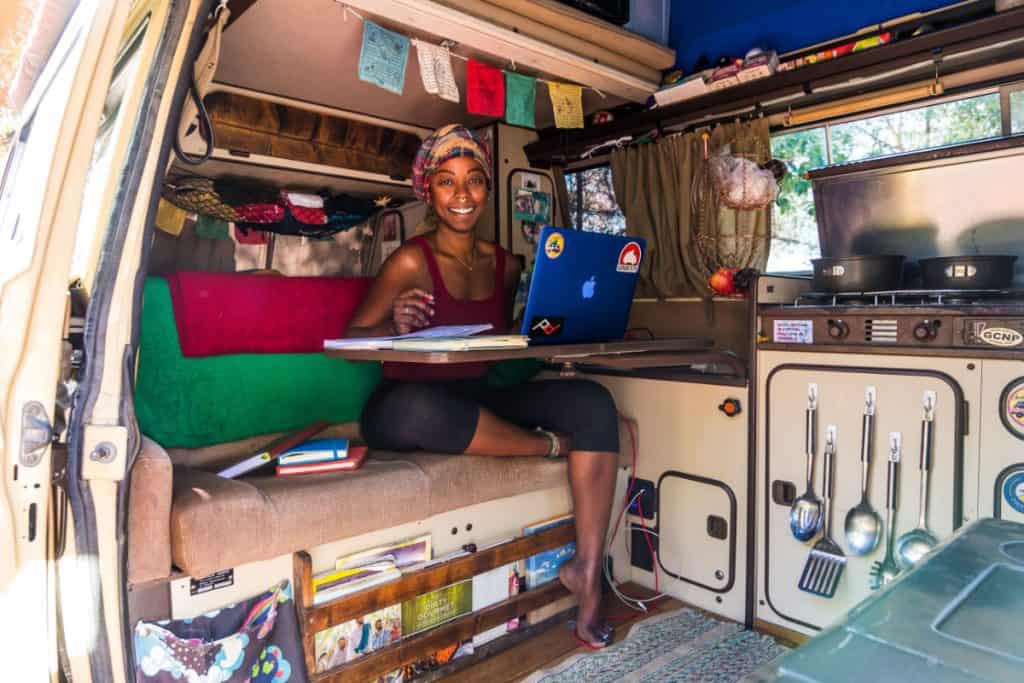 Woman works at a laptop inside of a westfalia van