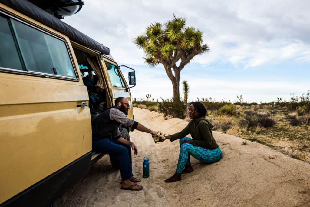 Man and woman hold hands outside of their campervan