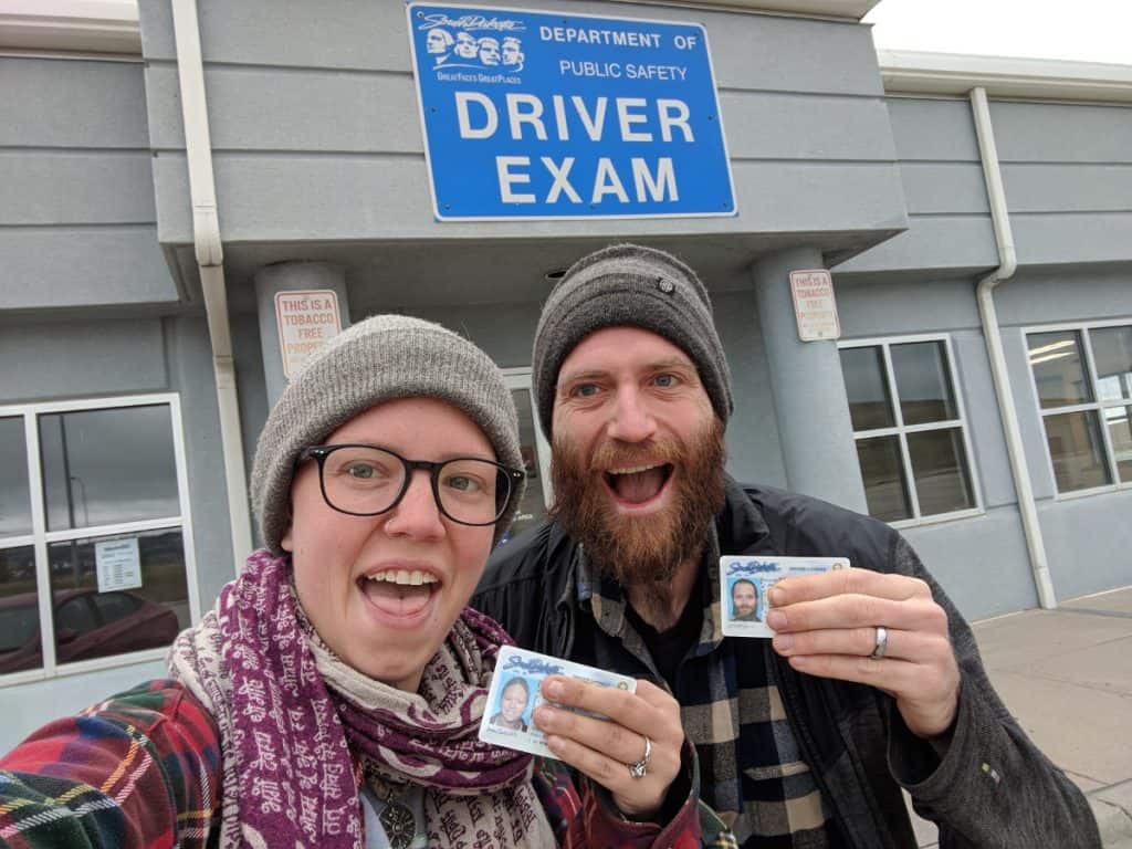 John and Jayme stand outside the DMV, holding their new South Dakota licenses and looking happy