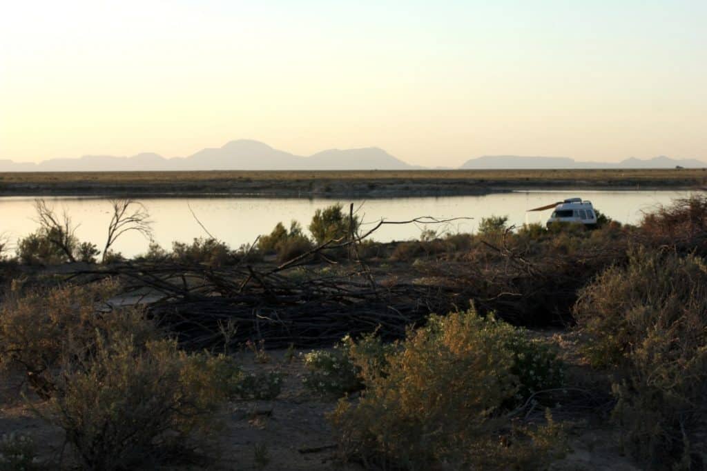 Van is parked in a quiet and secluded area on the water. There are mountains in the distance far past the water.