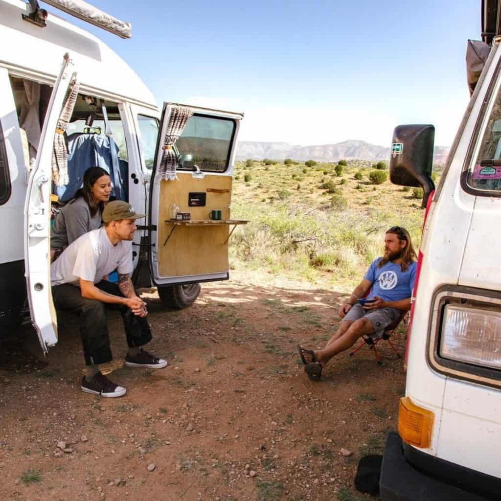 One girl and two guys sit around their vans chatting in the Arizona desert.