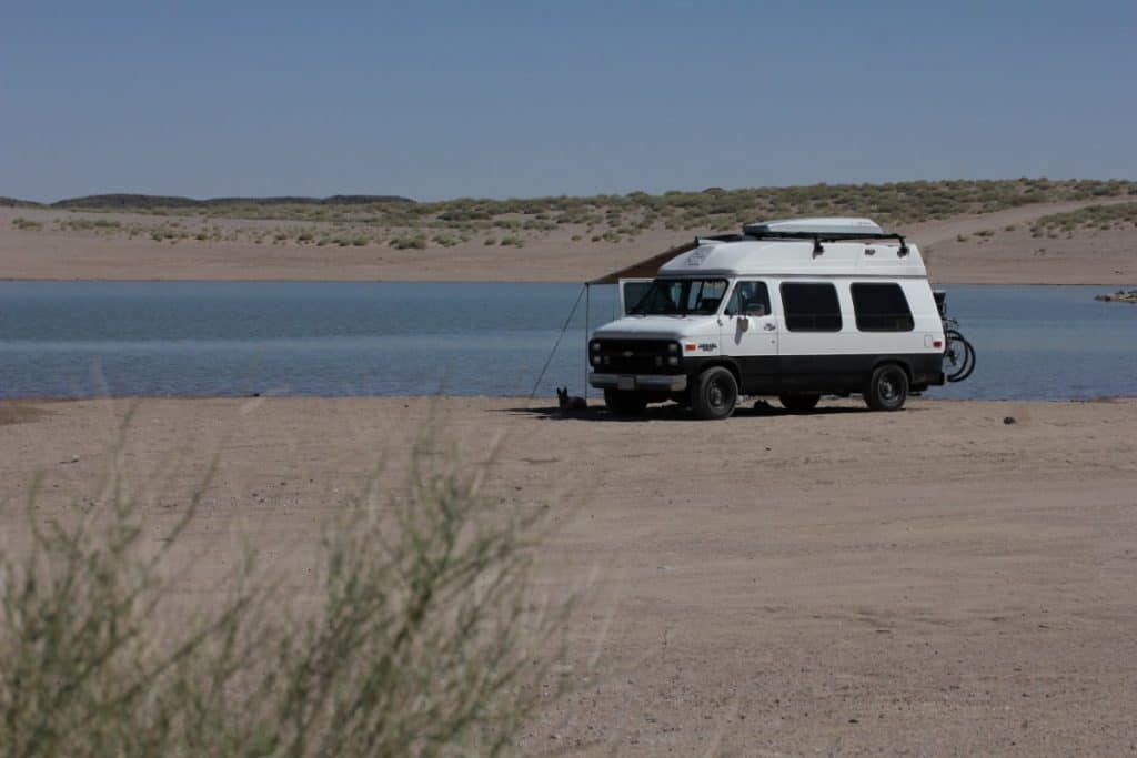 Van sits on a beach with the water right outside of it's open doors. Seems to be the only rig on the beach.