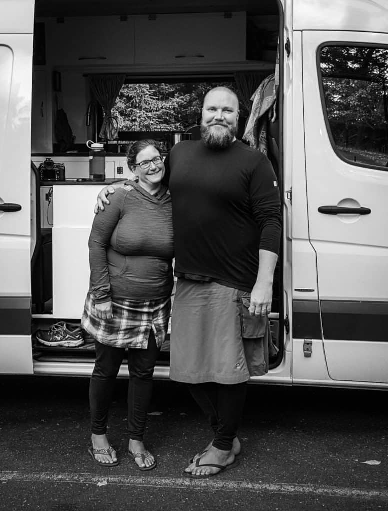 Man and woman happily pose in front of their white Sprinter van. The photo is in black in white.