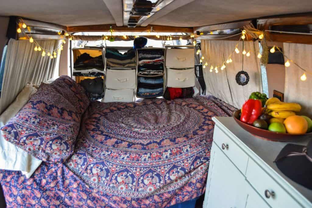 The interior of a van built into a tiny home. We see a large bed and clothing storage near the back of the van.