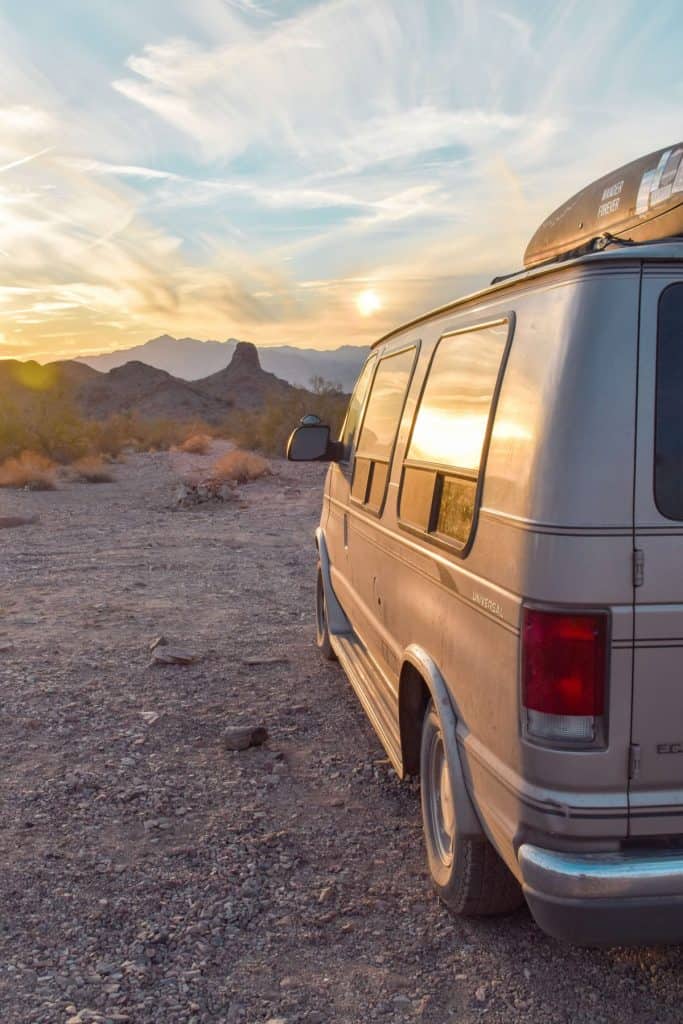 Side view of the van from the back side to the front of the van, just past the front the sun sets over a mountain range.