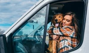 girl and dog hugging on driver seat of van