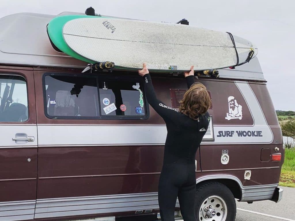 Man mounting surfboard to side of van