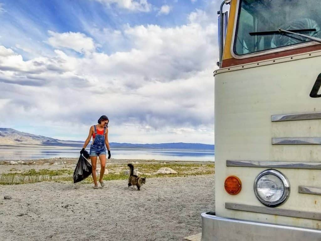 a woman walks alongside her dog carrying a bag of trash