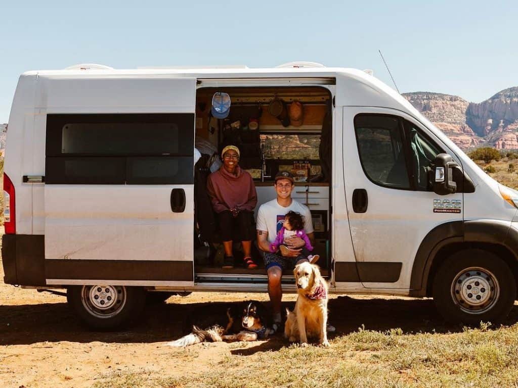 family with baby and dogs pose with van