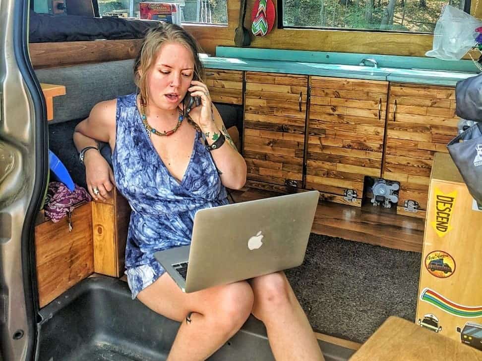 girl talking on phone and working in laptop in van