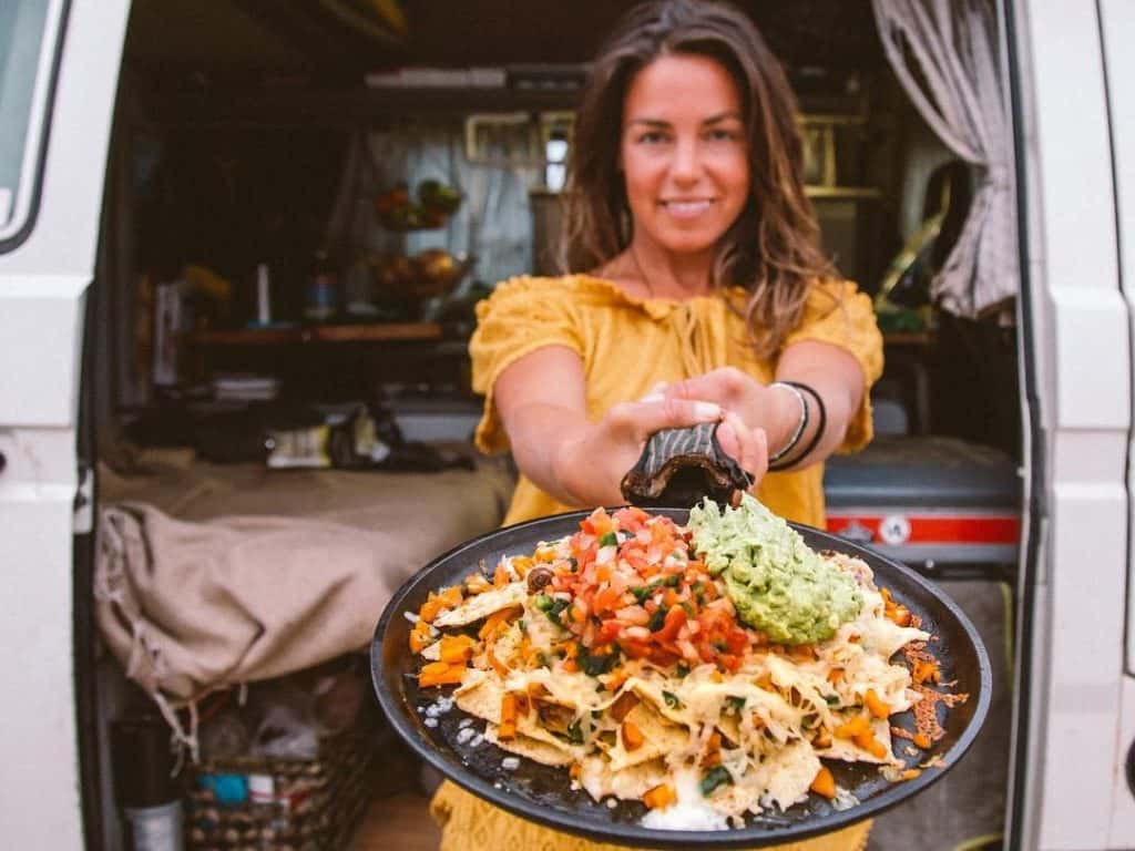 woman holds skillet of food outside of van