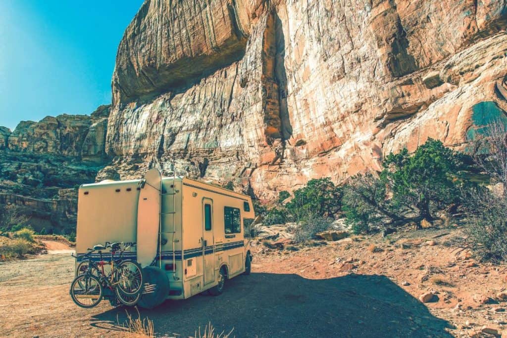 class c rv with mountain bikes mounted on the back parked by a rock face