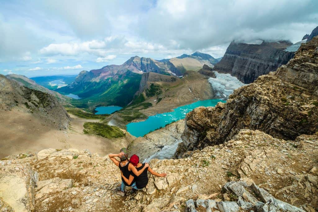 Nat & Abi look over many lakes and rivers and mountains as they stand at the top of a mountain.