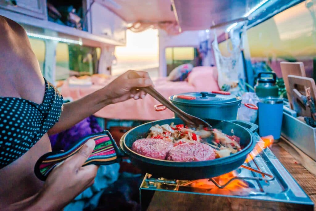 A close up of Nat cooking burgers and veggies in the van.