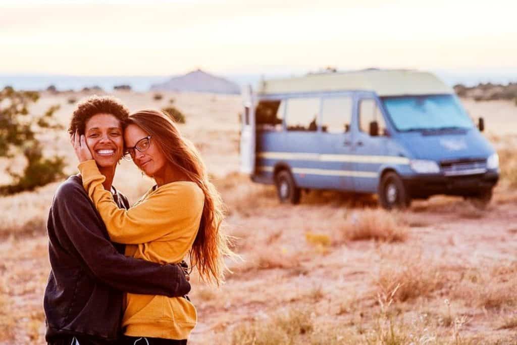 Abi and Nat lovingly embrace one another with the van in the background.