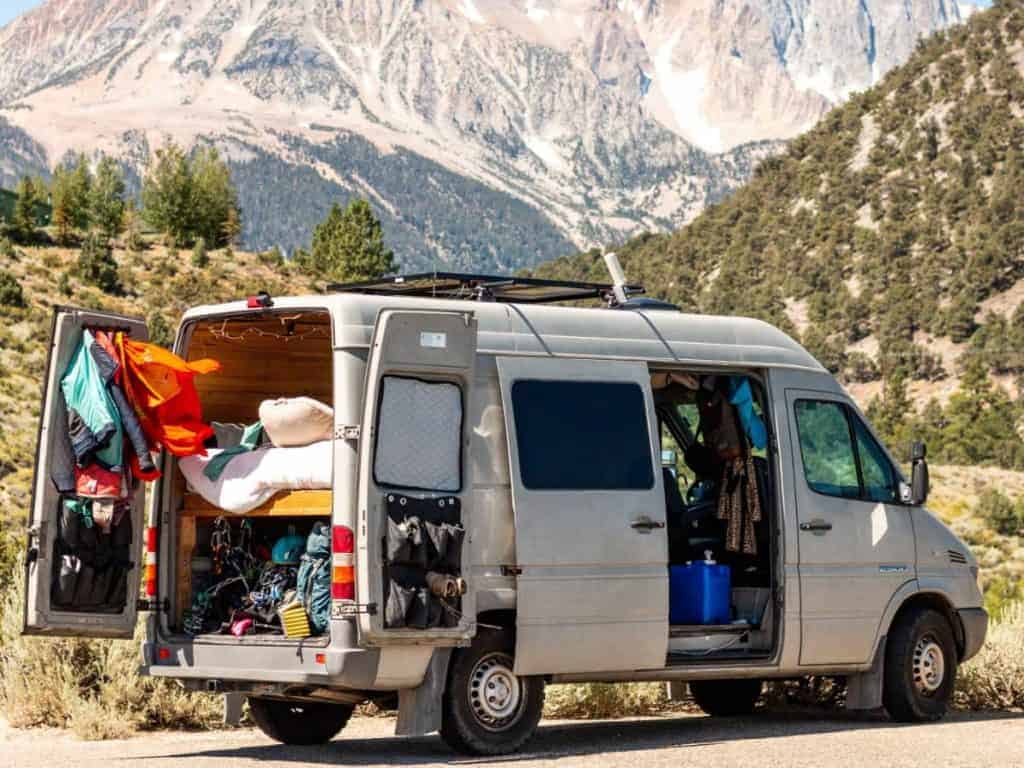 Van is parked with mountainous background with all of it's doors open exposing the storage.