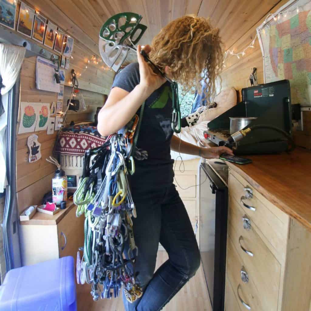 Kaya stands in the kitchen of her van holding cams and carabiners.