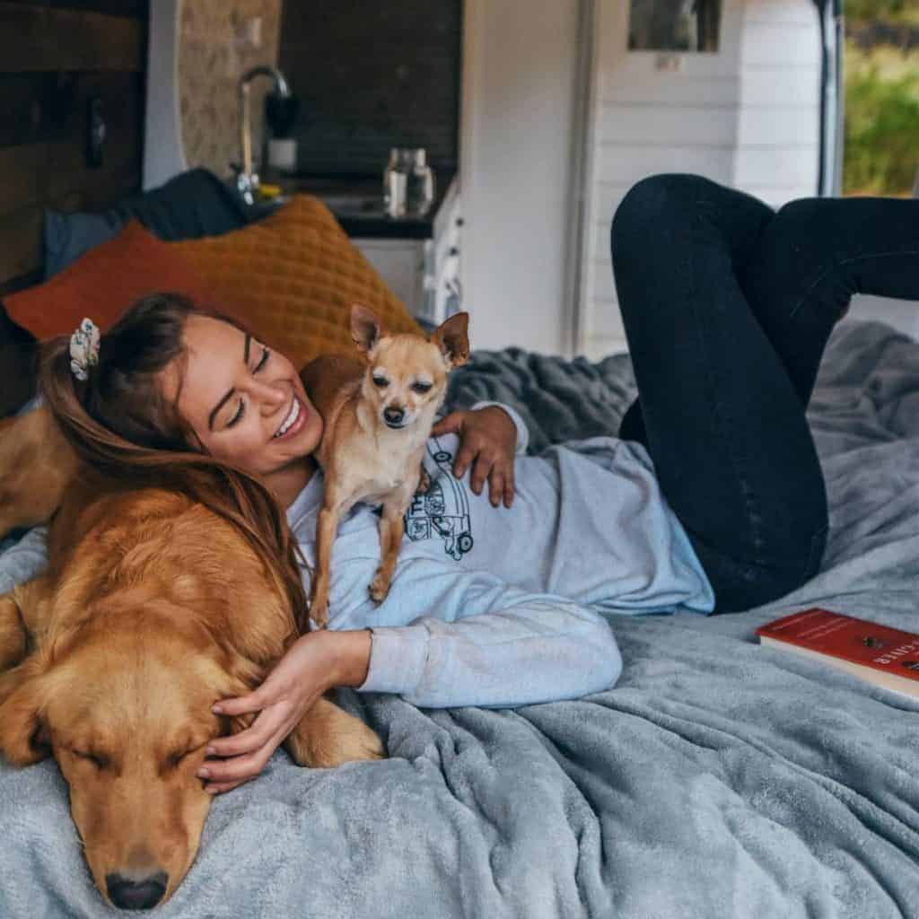 Sydney lies in bed with her head on her dog Ella and her other dog lies across her chest.