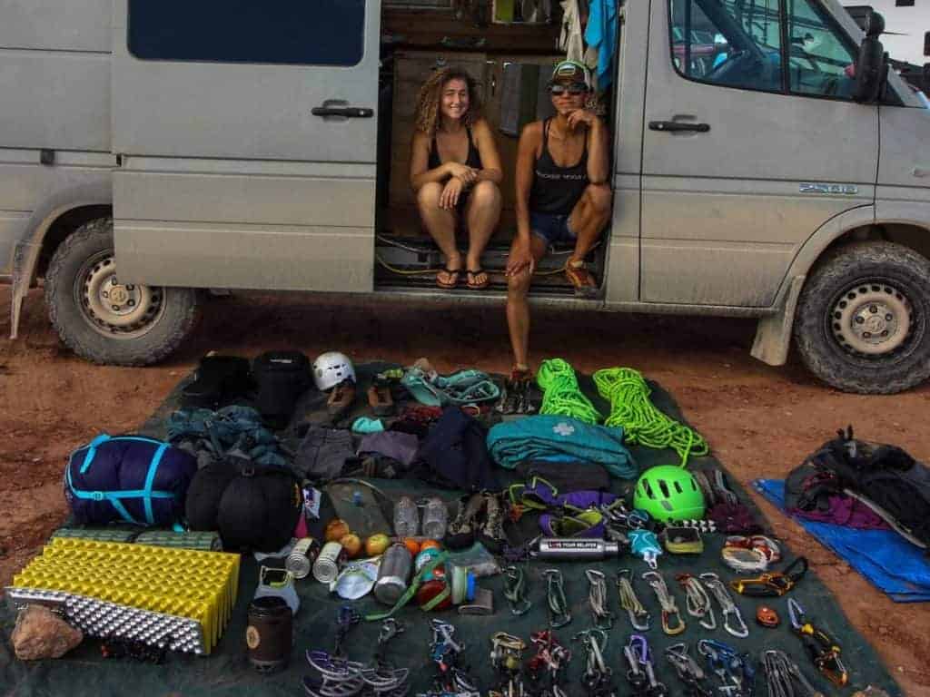 Two people sit on the side of Kaya's Sprinter with gear sprawled out on a tarp in front of them.