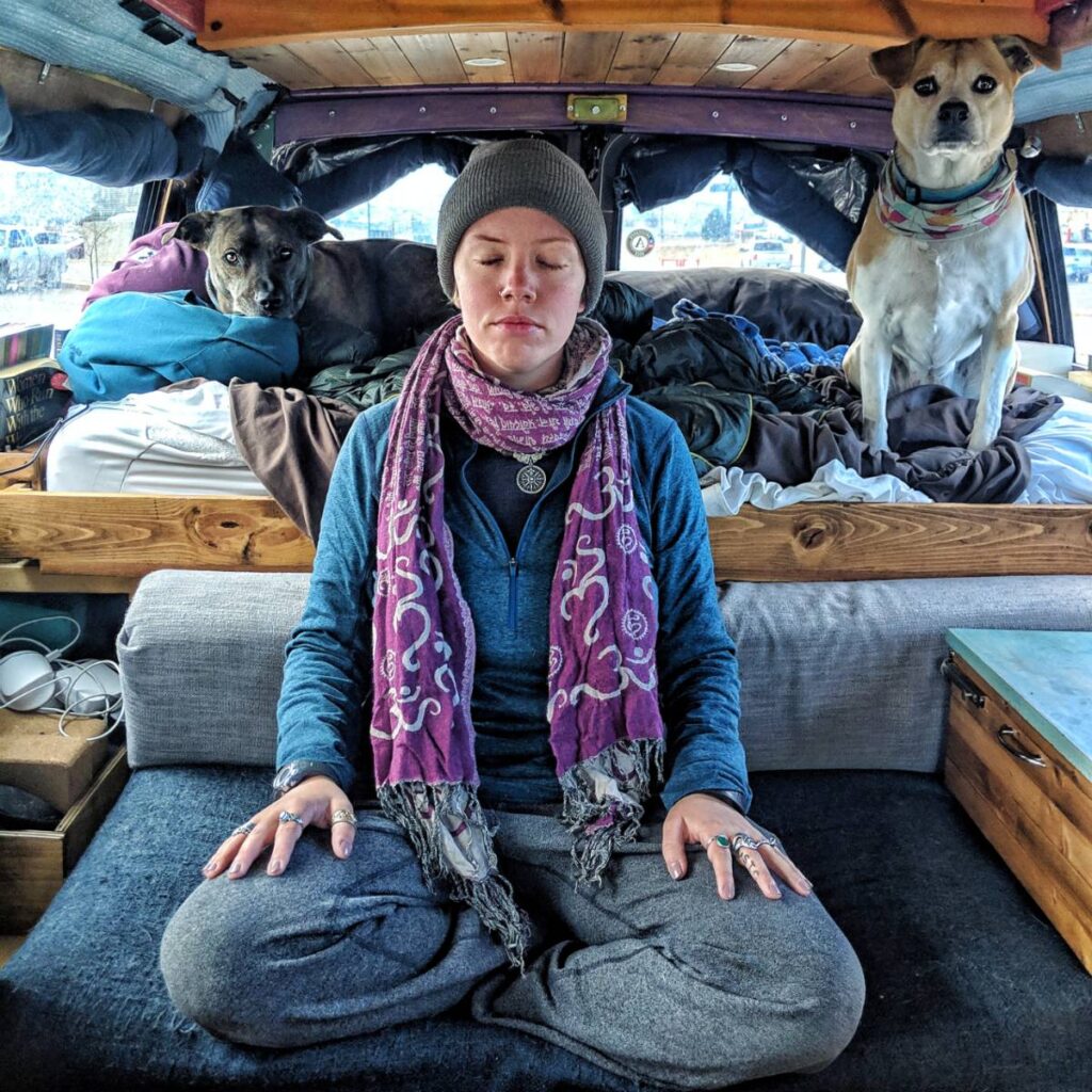 Jayme meditates on the couch. Delilah and Nymeria are both on the bed behind her, looking at the camera.