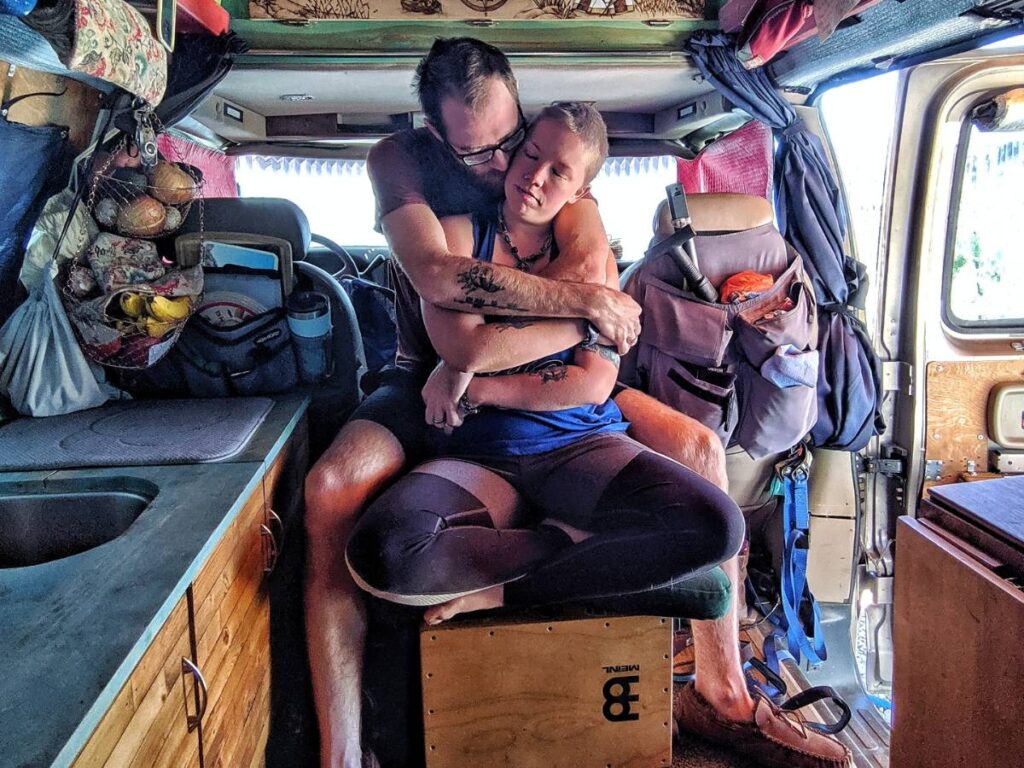 Jayme sits on the cajon cross-legged as John holds her from behind.