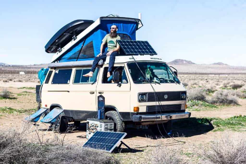 Dustin sits on the roof of the van next to the solar panel.