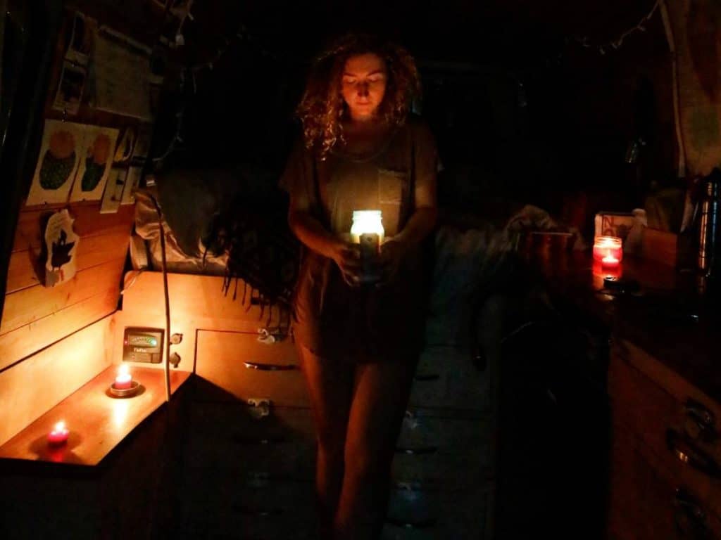 Kaya holds a candle, standing in the darkness of her van, surrounded by more candles.