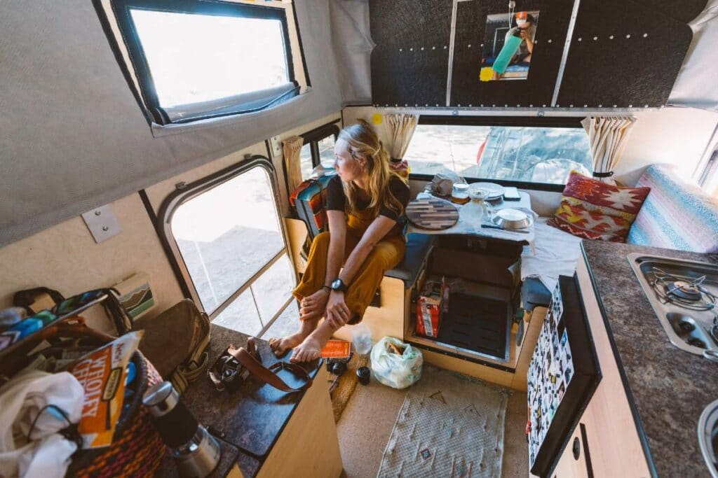 Intérieur du campeur. Une femme est assise sur la banquette de la dinette et regarde par la porte ouverte