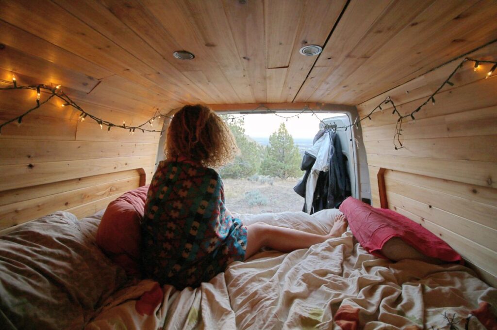 Woman sitting on bed inside Sprinter van looking out the back doors