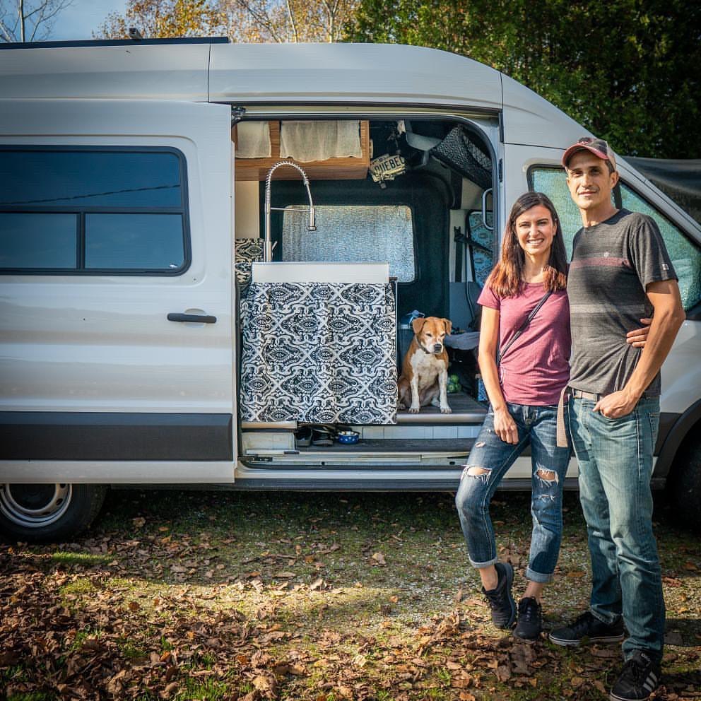 @doriandmena couple standing behind ford rv van with a dog inside