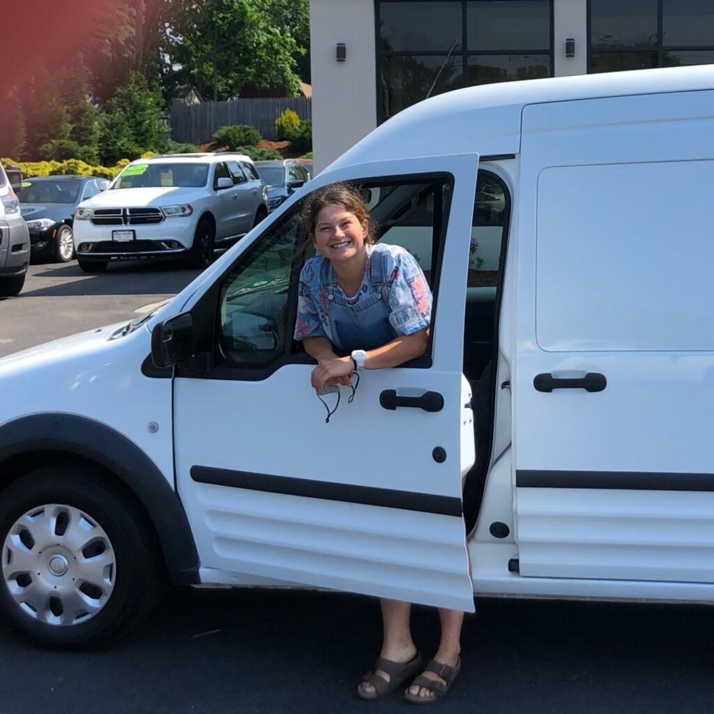 @eee_vanstagram Smiling woman standing by the door of a white ford transit connect camper van