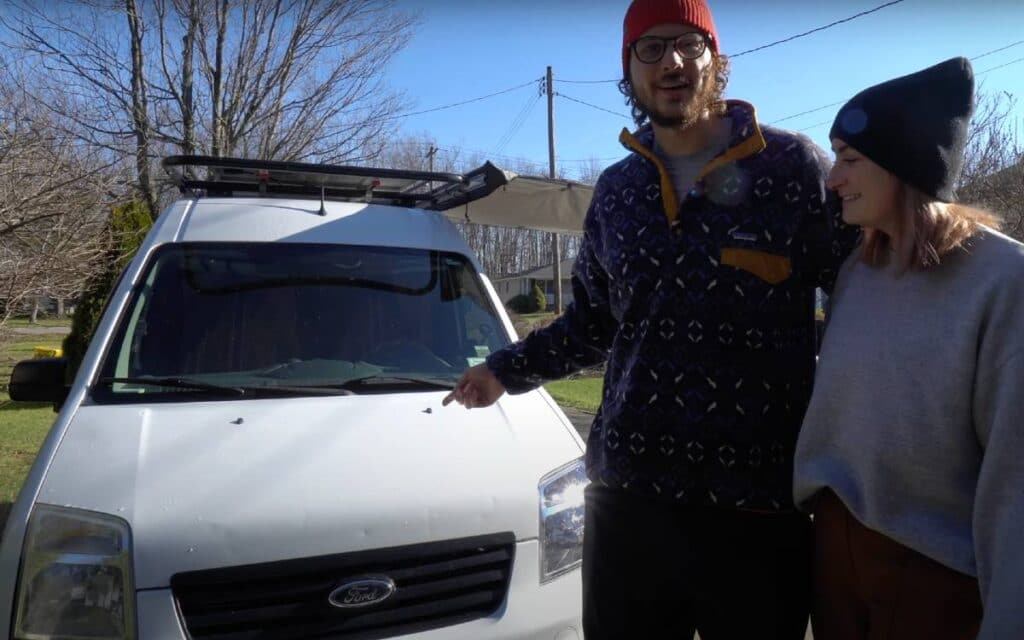 @mikeandheathervlog Couple standing next to a white ford transit connect campervan