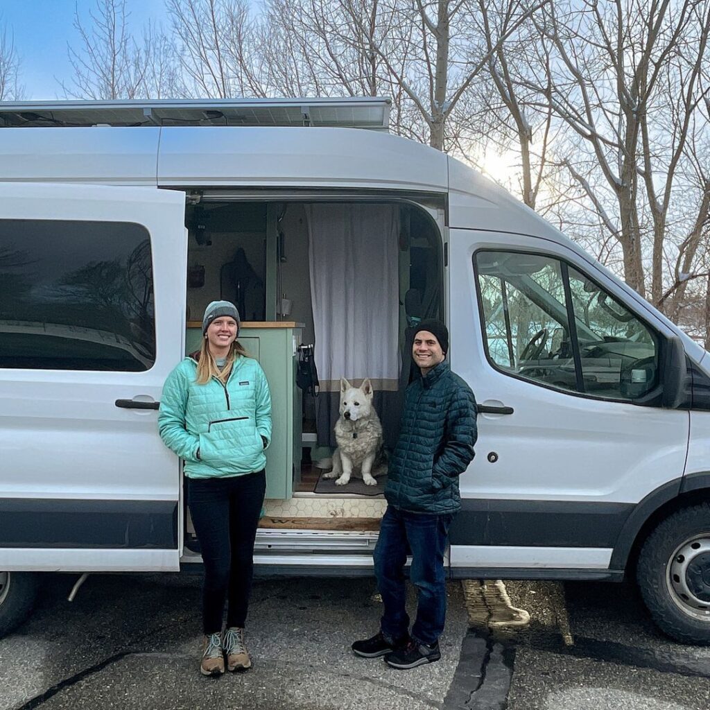 @stokeloafvan couple standing against a ford transit camper van with their dog sitting in the doorway