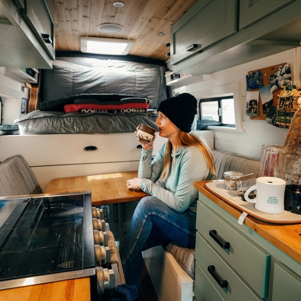 @stokeloafvan woman sitting inside ford rv van looking outside the window while drinking coffee