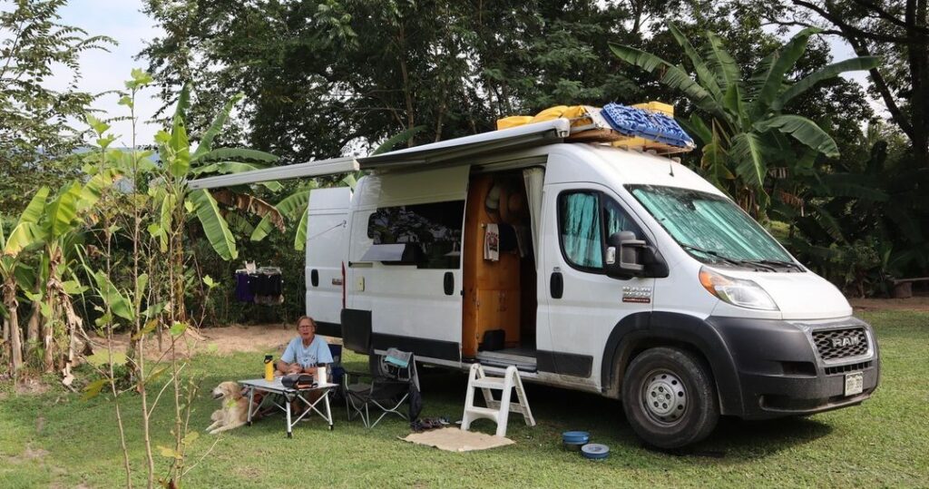 @clarity.offgrid Man with his dog sitting in a camping chair next to his camper van