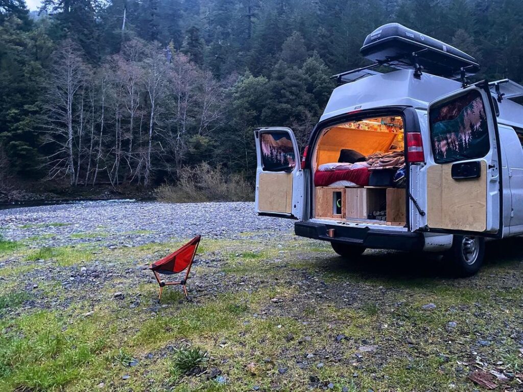 @dylventures White chevy express camper van parked in the forest with its back door open