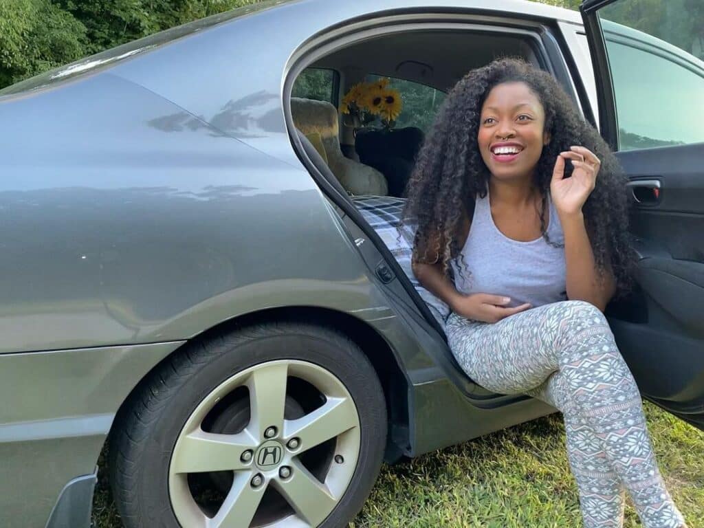 @mothernateur Smiling woman sitting in the open door of her camper car