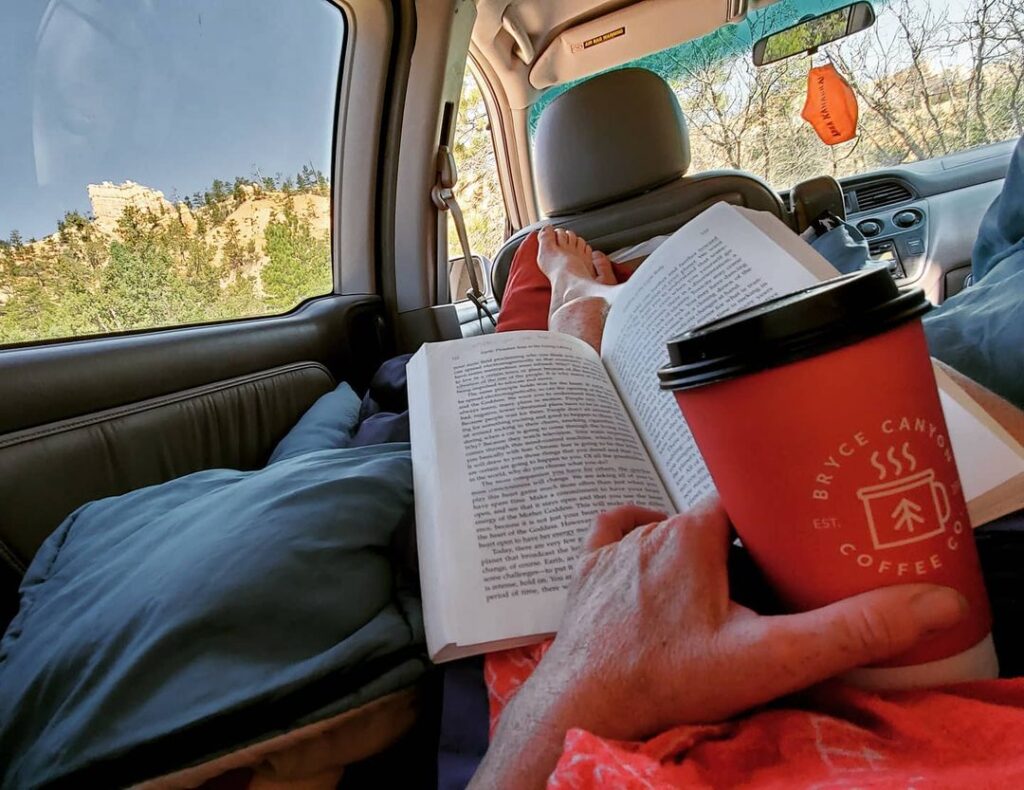 @solsticeelliott drinking coffee and reading a book in minivan rv