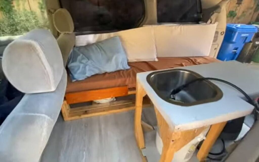 A bed next to a sink inside a converted Toyota Sienna