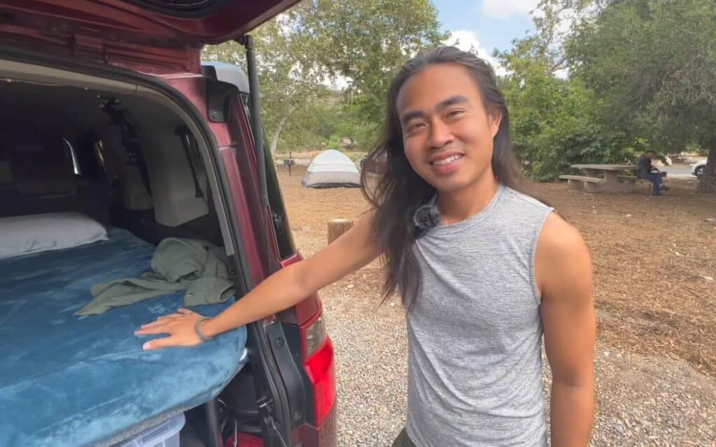 Hao smiling at the camera while standing next to his honda element camper