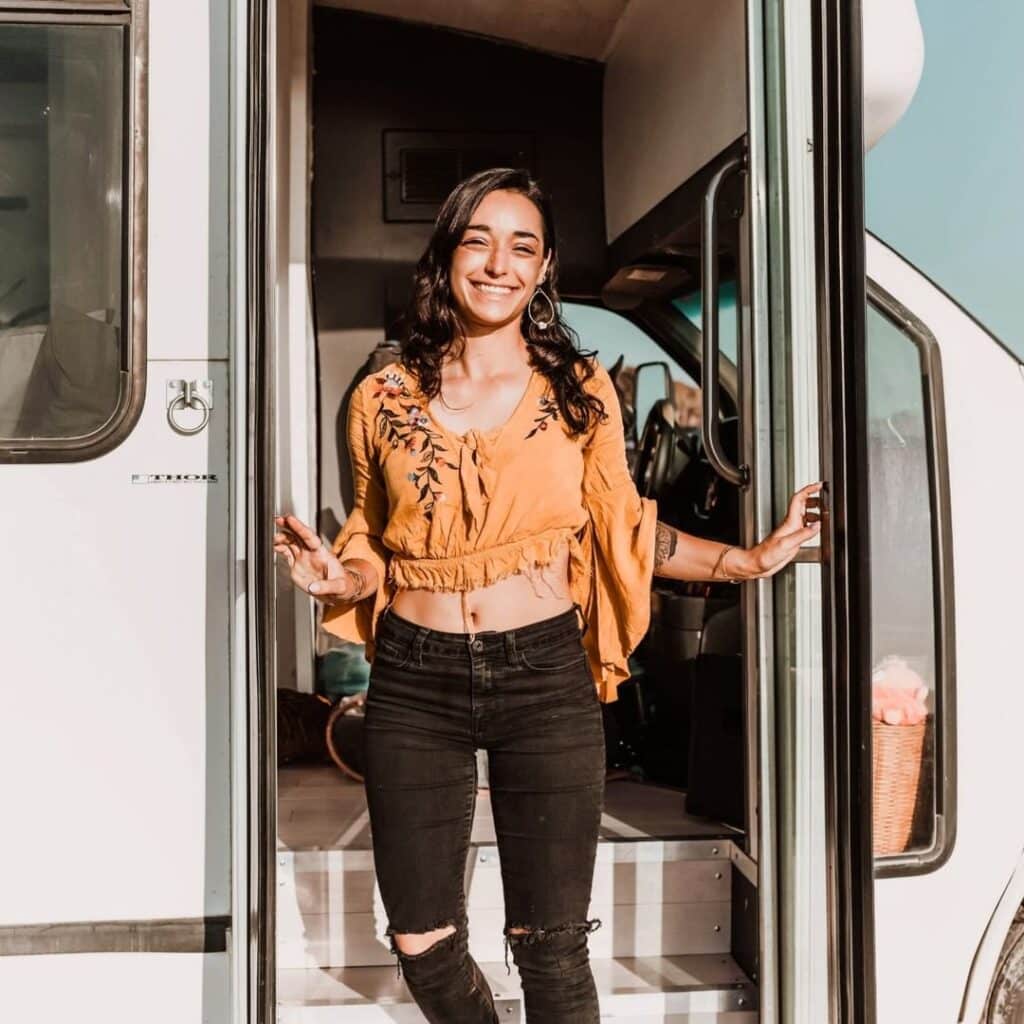@thegloriaceleste Gloria smiling at the camera while standing in the doorway of her minibus rv