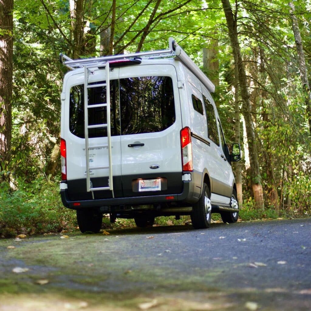 Back view of a White AWD campervan parked on the roadside in the forest