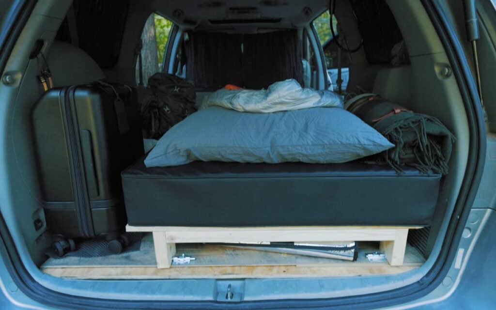 Bo's camper van bed next to a black luggage and backpack