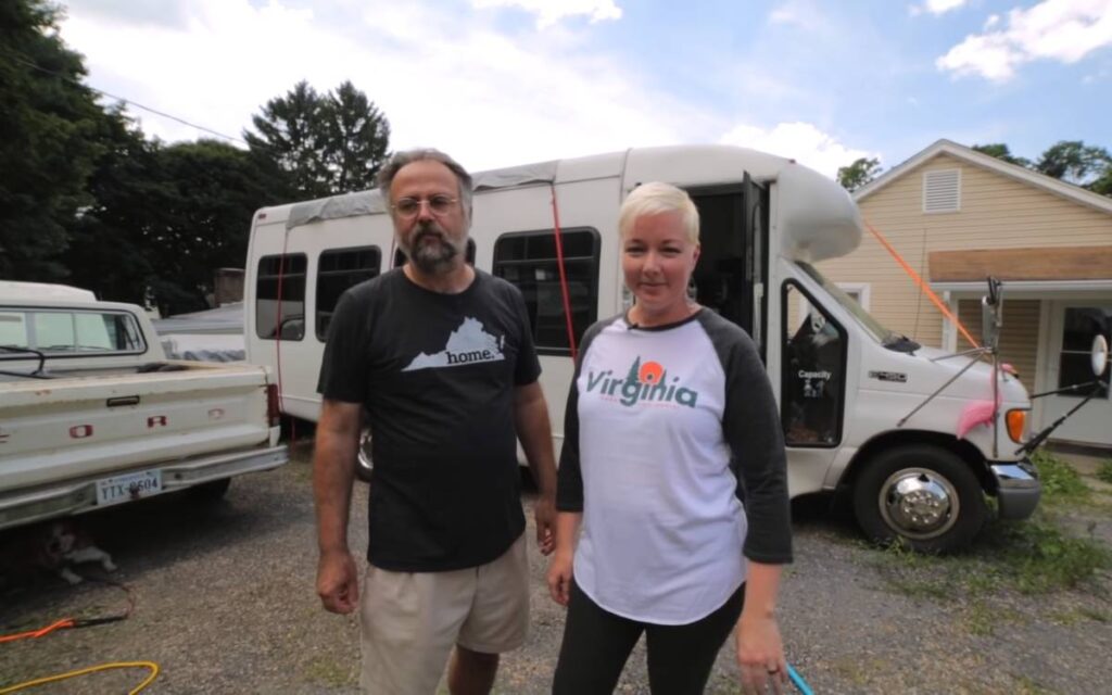 Carmen and Xaver standing next to their tiny home, giving a tour of their shuttle bus rv conversion