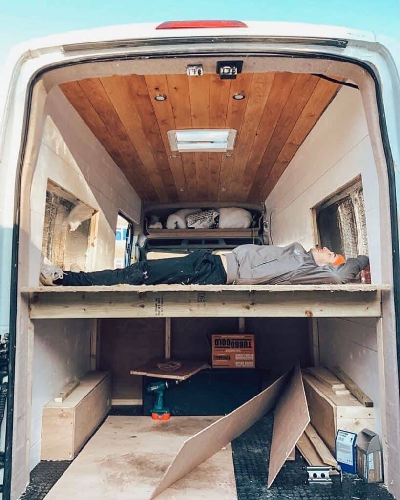 Man Lying On His Back Inside An Unfinished Camper Van 819x1024 