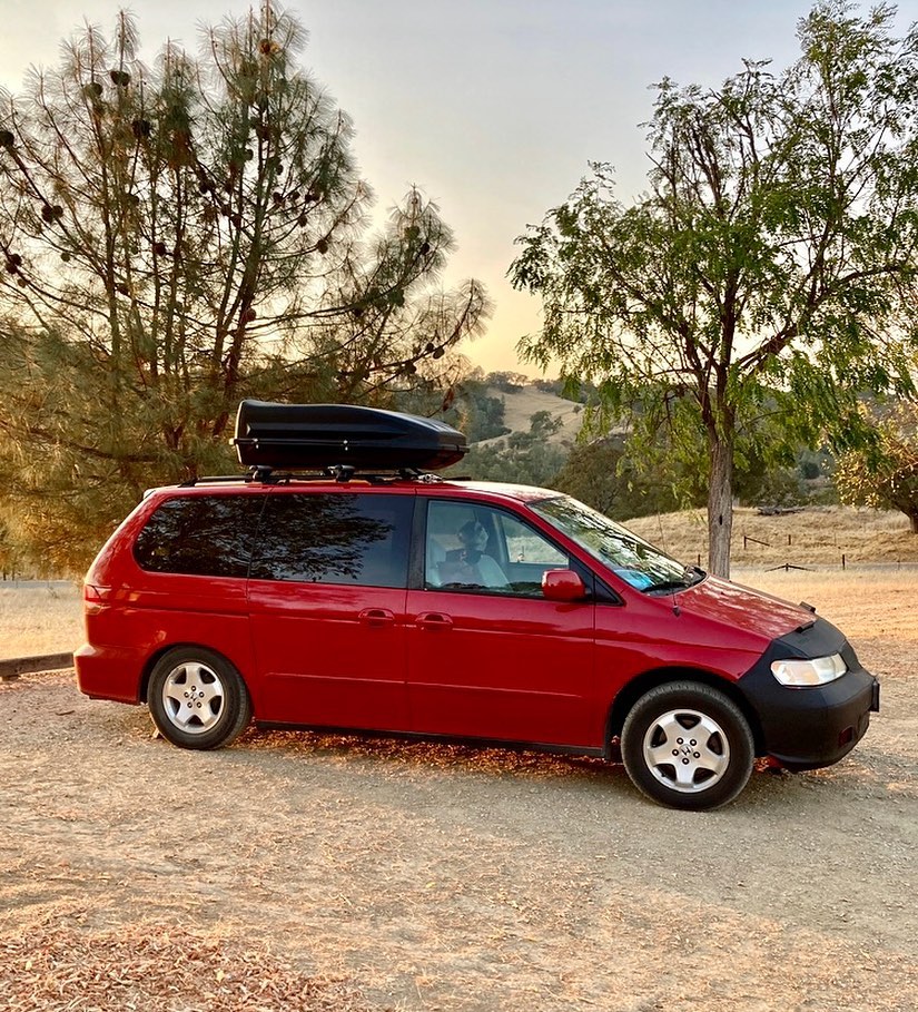 Red minivan camper parked on unpaved road